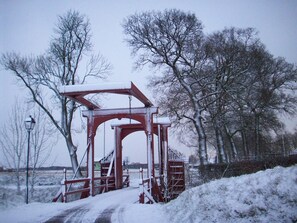 A snow-covered pedestrian bridge in a park with bare trees and a lamppost. - Hotel Borchers (Doerpen)