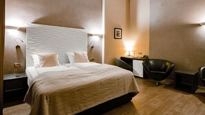 A modern hotel room with a large bed, two bedside tables, a desk, a chair, and a wall-mounted lamp. - Artim Hotel (Berlin)
