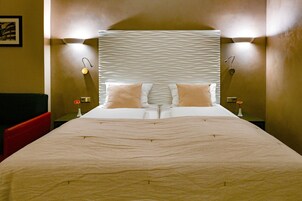 A neatly made bed with a patterned headboard, two bedside lamps, and a vase with a flower on each nightstand.