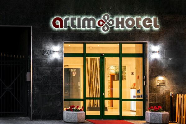 Das Hotel von außen mit einem großen Glas Eingang, einem Namensschild darüber und einem roten Teppich, der zur Tür führt.