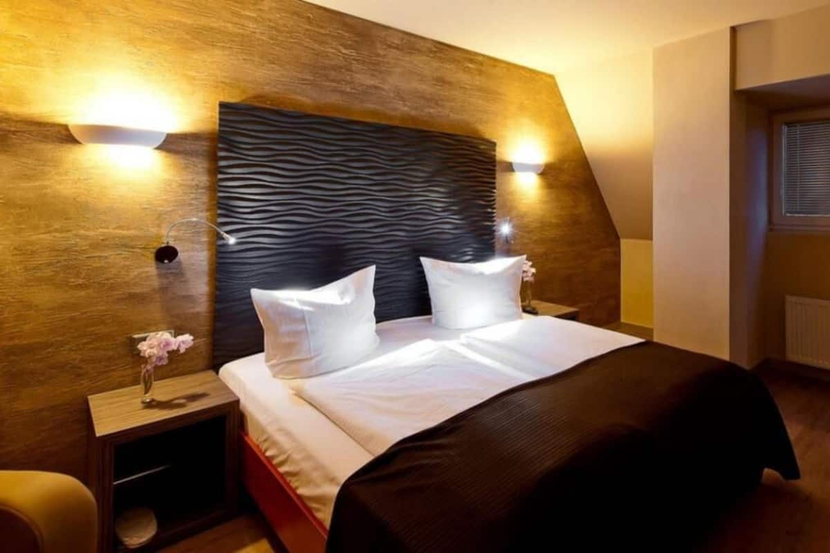 A hotel room with a bed, nightstands, a vase with flowers, and a unique textured headboard.