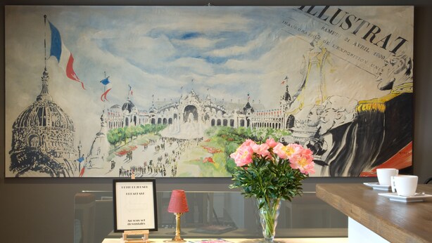 Un mostrador de recepción con un gran mural ilustrado, un certificado enmarcado, una lámpara roja y un jarrón de flores.