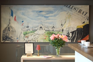 Un mostrador de recepción con un gran mural ilustrado, un certificado enmarcado, una lámpara roja y un jarrón de flores.