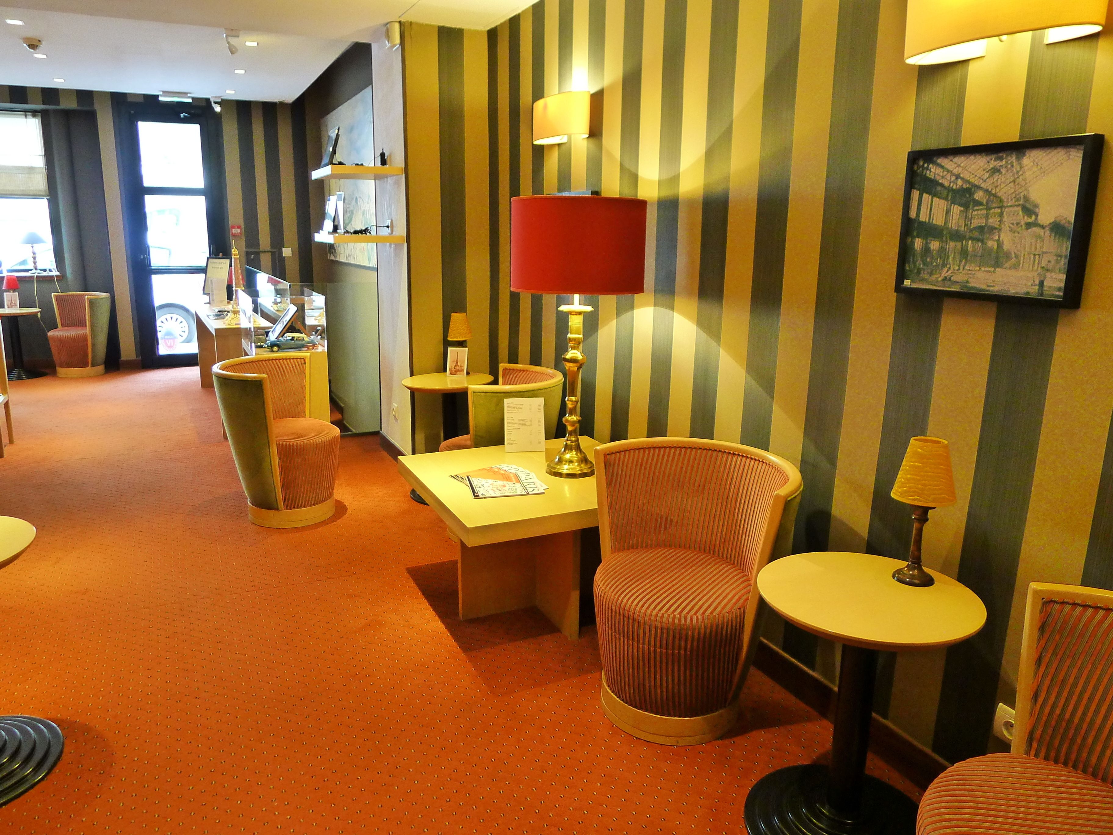 A hotel room with striped wallpaper, a red lamp, and a small table with a chair.