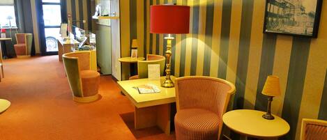 A hotel room with striped wallpaper, a red lamp, and a small table with a chair.