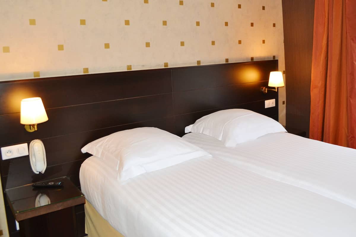 Quarto de hotel com cama bem arrumada, duas luminárias de cabeceira, um telefone e uma janela com cortinas.