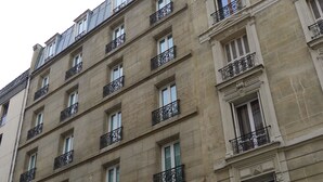 Un edificio de varios pisos con balcones, un letrero que dice 'Leamans & Fure' y un letrero que anuncia 'Cours de Guitare'.