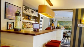 Zona de bar con taburetes, estantes con botellas, un cuadro enmarcado y una lámpara.