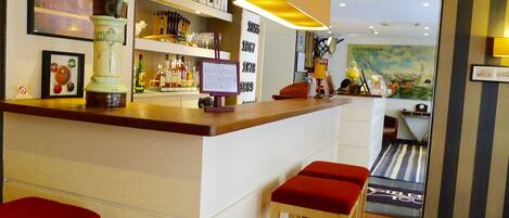 A bar area with stools, shelves with bottles, a framed picture, and a lamp.