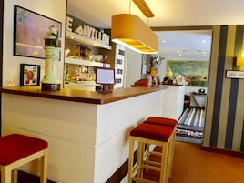 Zona de bar con taburetes, estantes con botellas, un cuadro enmarcado y una lámpara.