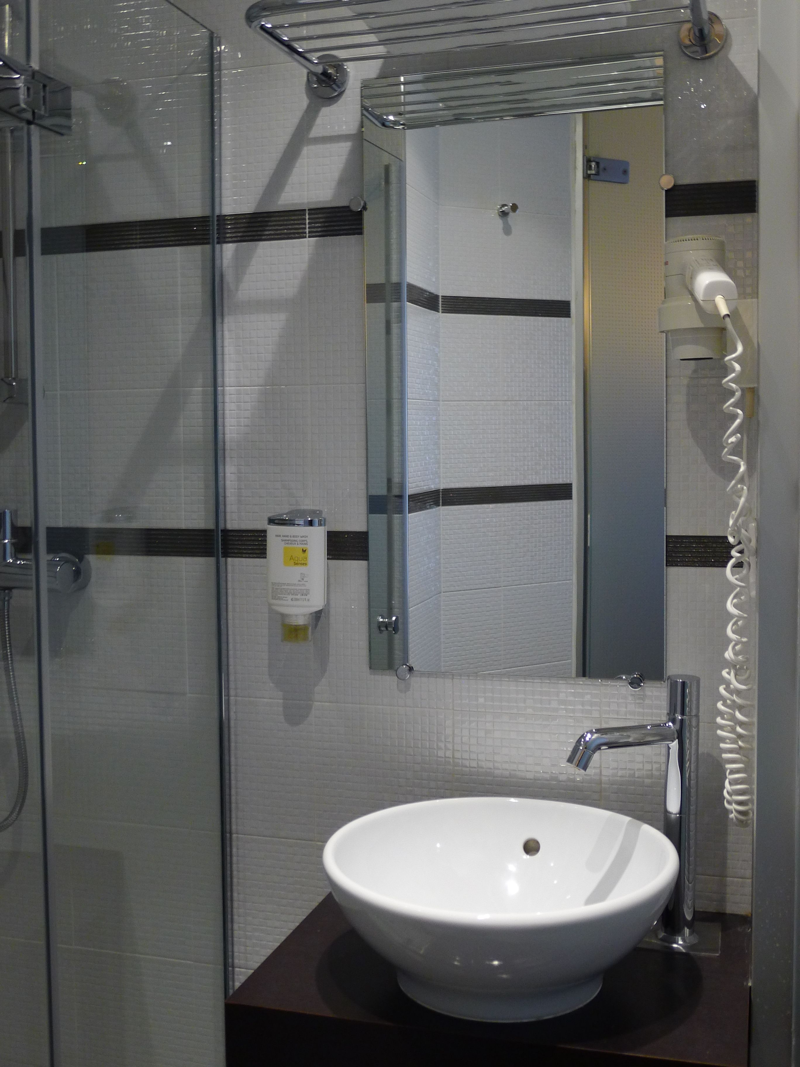 Un baño con ducha envuelta en vidrio, un lavamanos blanco y un espejo con toallero.