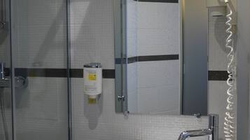 Un baño con ducha envuelta en vidrio, un lavamanos blanco y un espejo con toallero.