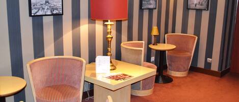 Un vestíbulo de hotel con papel tapiz a rayas, una mesa con una lámpara roja y dos sillas de mimbre.