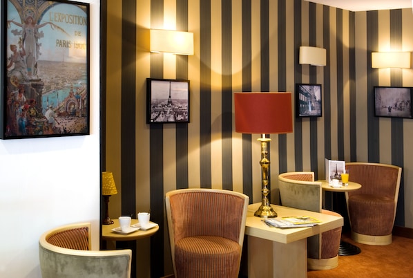 A hotel lobby with striped wallpaper, multiple chairs, a table with a lamp, and framed pictures on the wall. - Hôtel de l'Exposition Tour Eiffel (Paris)