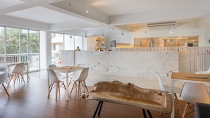 A spacious living area with a large wooden bench, white chairs, and a marble fireplace.