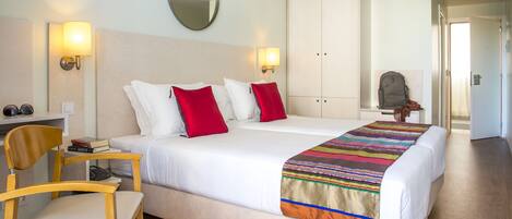 Una habitación de hotel con cama, dos mesitas de noche, una silla, escritorio, espejo y armario.