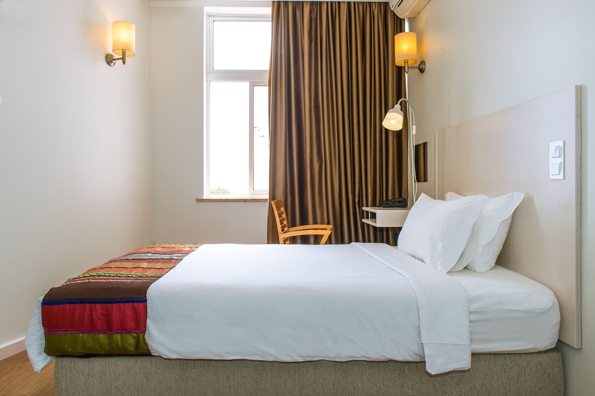 Una habitación de hotel con cama, escritorio, silla y ventana con cortinas.
