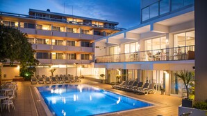 A hotel with a swimming pool, multiple balconies, and lounge chairs.