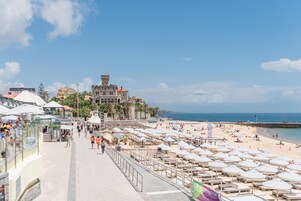 Um calçadão à beira-mar com guarda-sóis, um restaurante e um edifício histórico ao fundo.