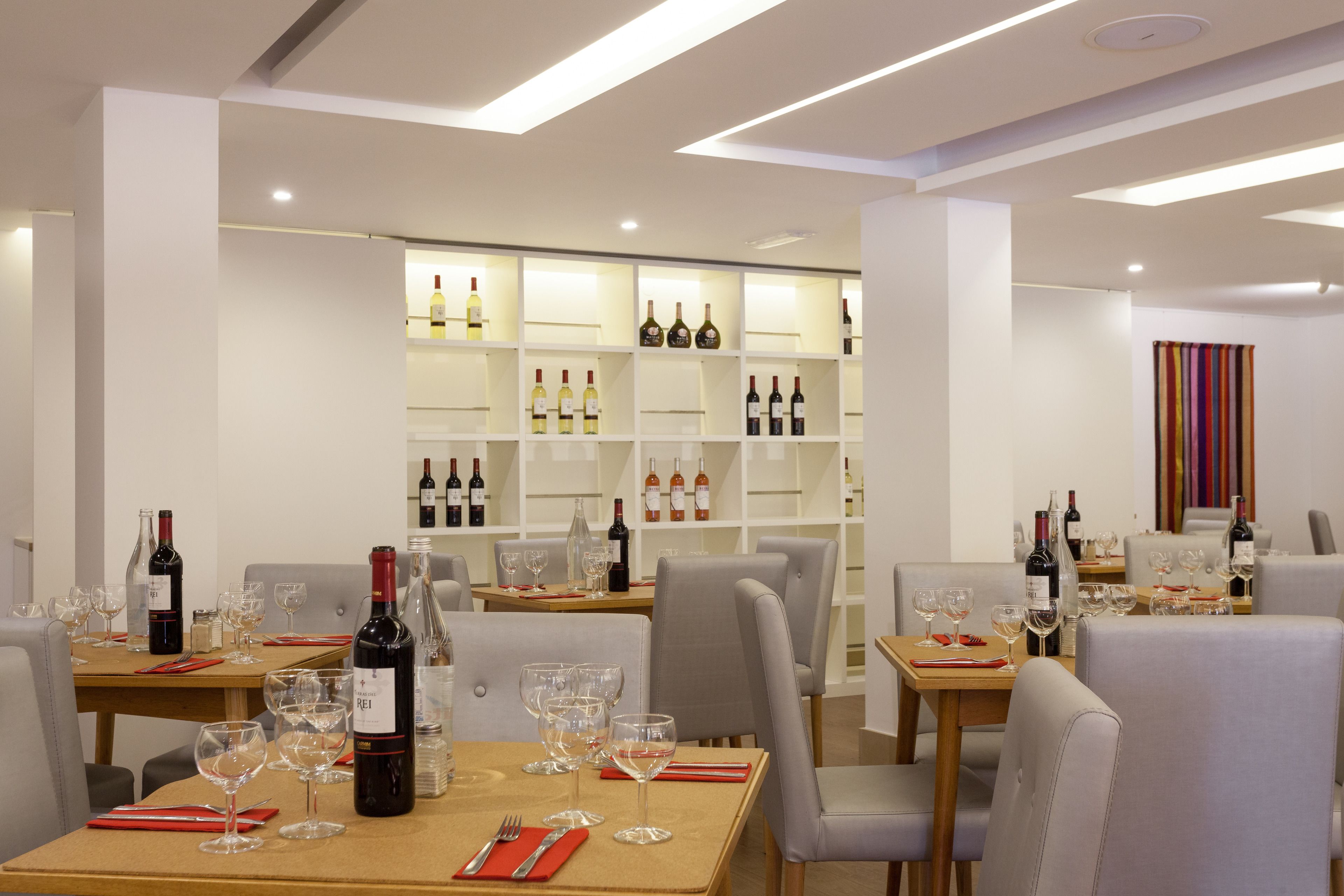 A restaurant interior with tables set for dining, wine bottles on shelves, and a striped curtain in the background.