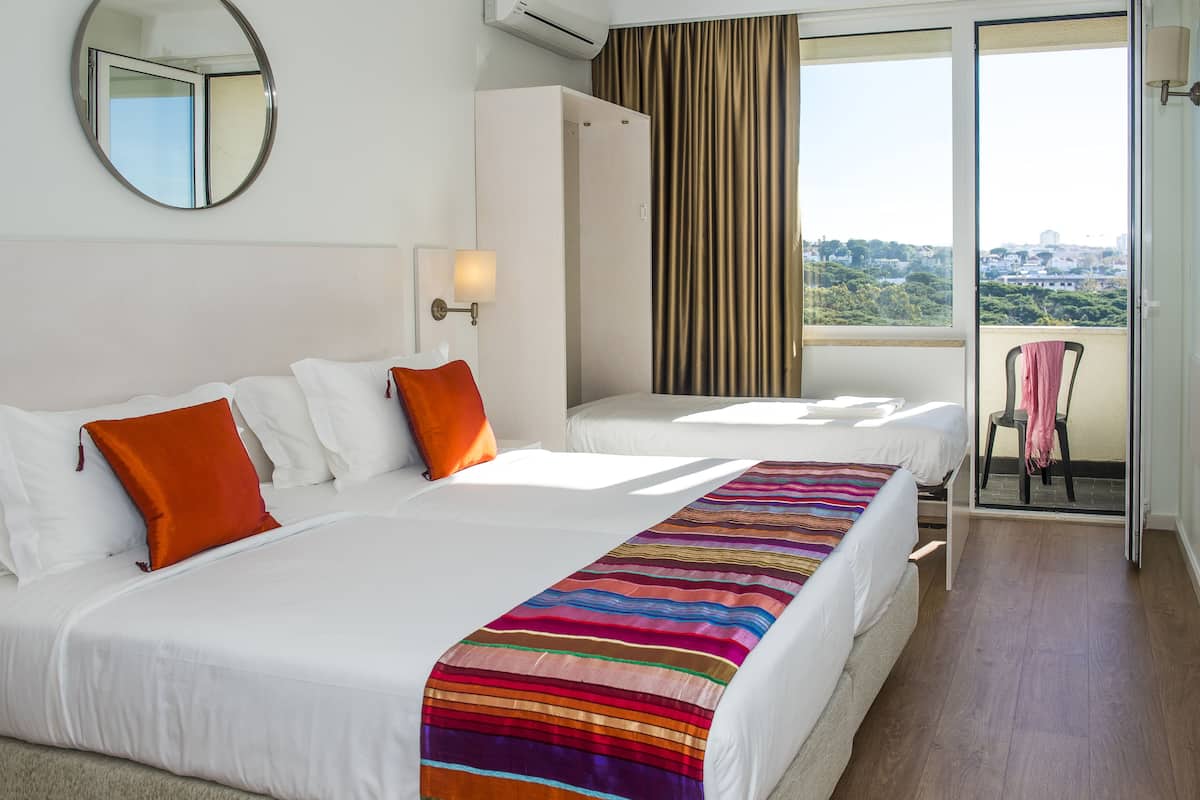 Habitación de hotel con dos camas, un espejo grande, una ventana con cortinas y vistas a la ciudad.