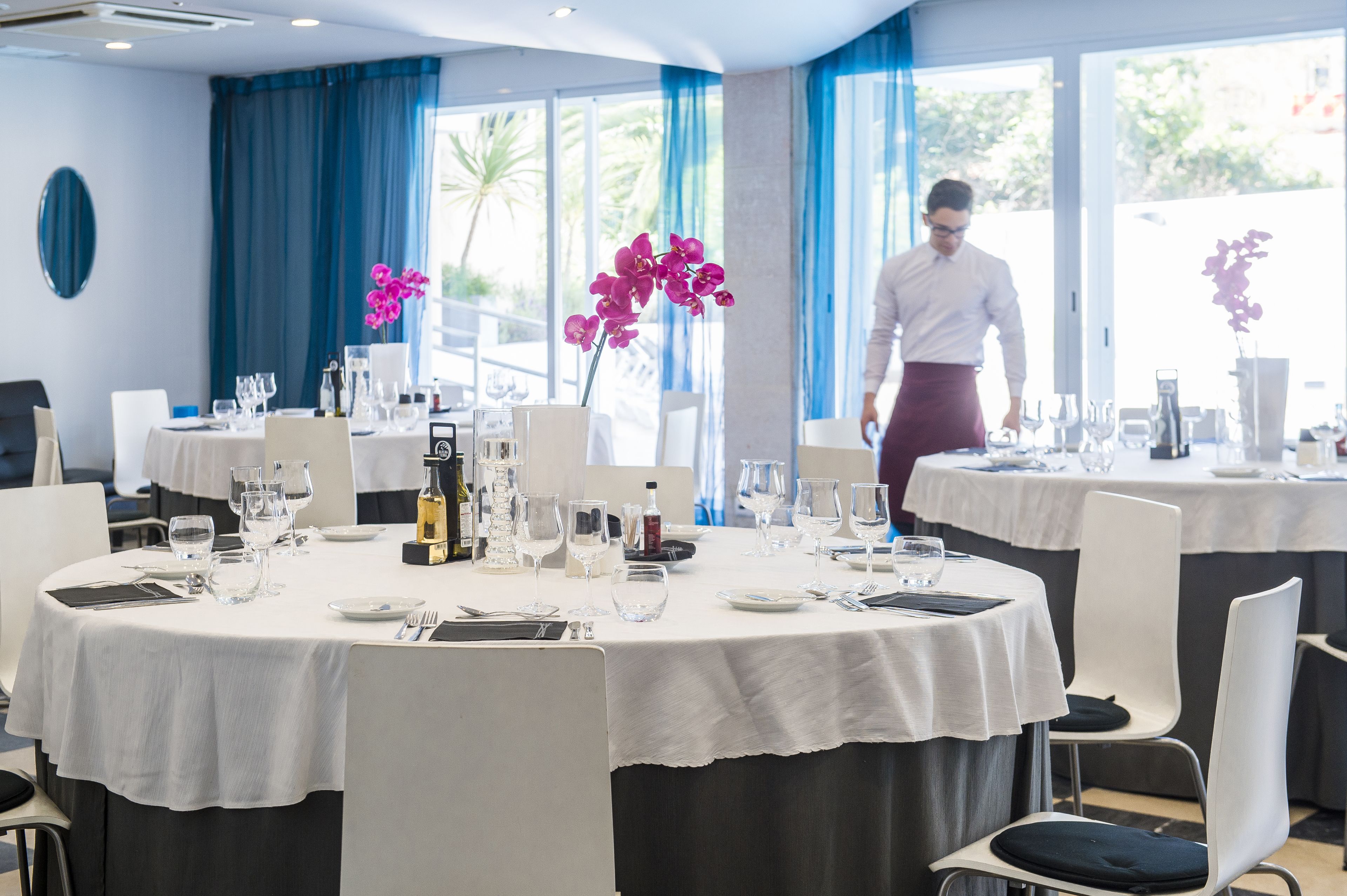 A restaurant with round tables, white tablecloths, and purple orchids.