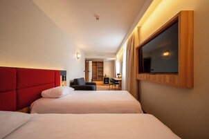 Habitación de hotel con dos camas, un televisor montado en la pared y un escritorio con una silla.
