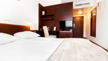 A hotel room with a large bed, a flat-screen TV, a wooden cabinet, and a desk with a chair.