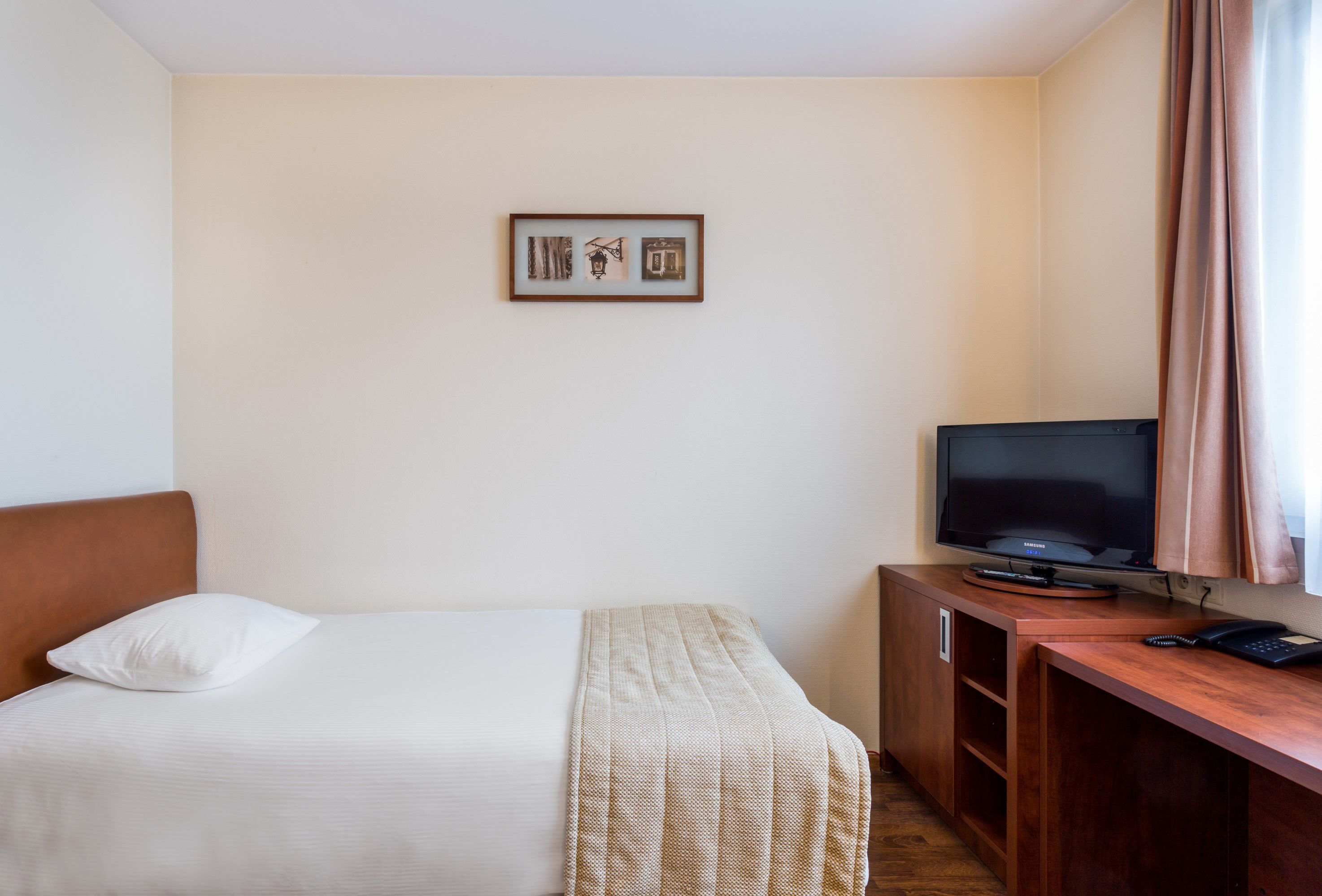 Habitación de hotel con una cama, un televisor sobre un escritorio de madera y un cuadro en la pared.