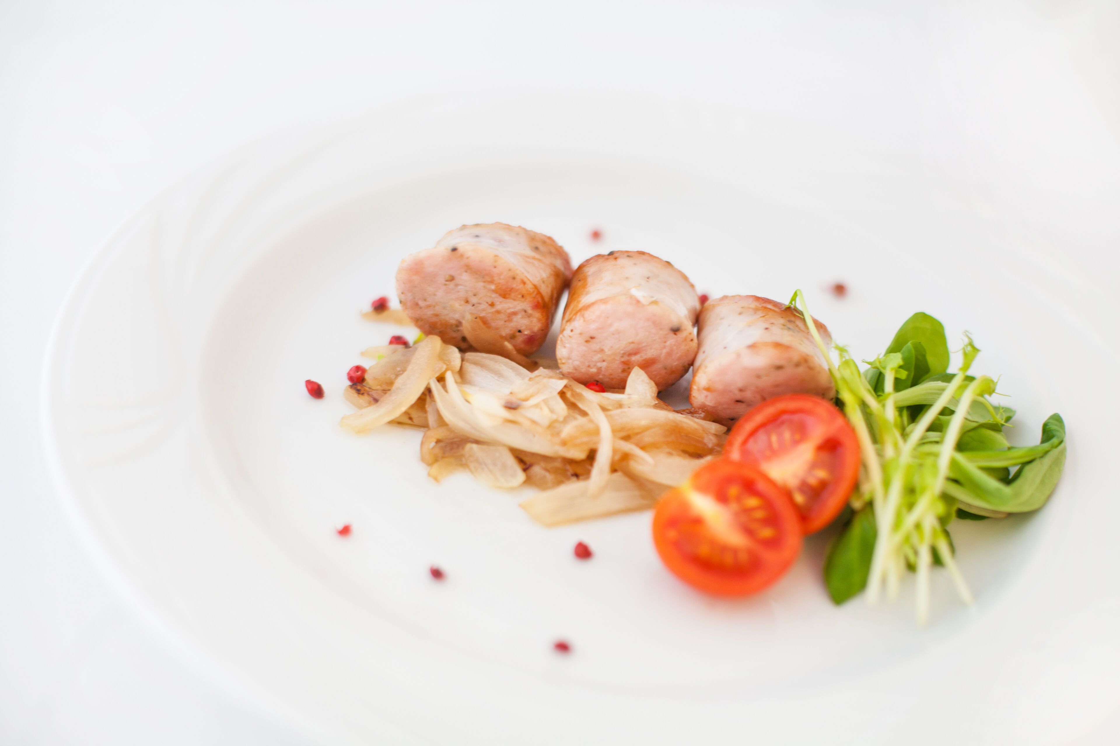 A white plate with three round meatballs, sliced onions, cherry tomatoes, and a small bunch of green leaves.