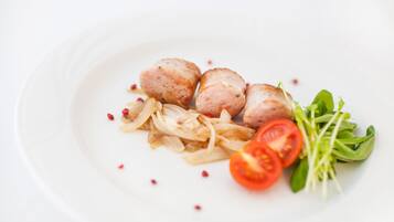 A white plate with three round meatballs, sliced onions, cherry tomatoes, and a small bunch of green leaves.