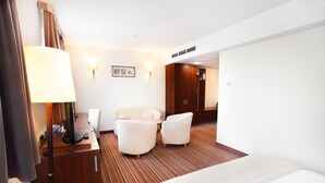 Habitación de hotel con cama, escritorio con computadora, dos sillas, lámpara y televisor montado en la pared.