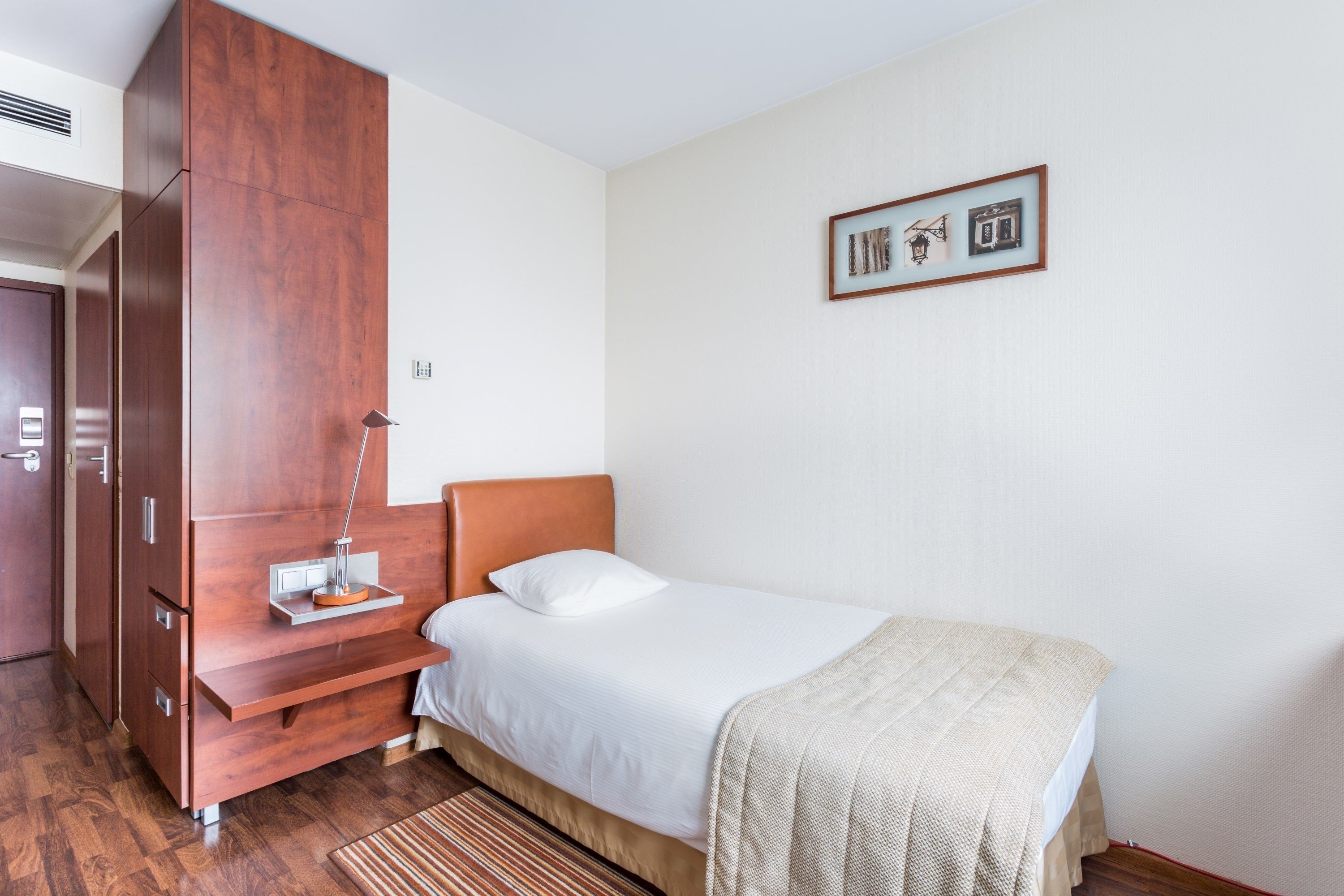 A hotel room with a bed, a bedside table, a lamp, a wardrobe, and a framed picture on the wall.