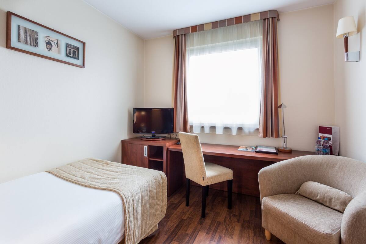 A hotel room with two beds, a desk with a computer, a chair, and a lamp.