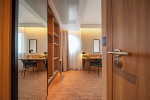 Habitación de hotel con armario de madera, escritorio con silla, espejo y piso alfombrado.
