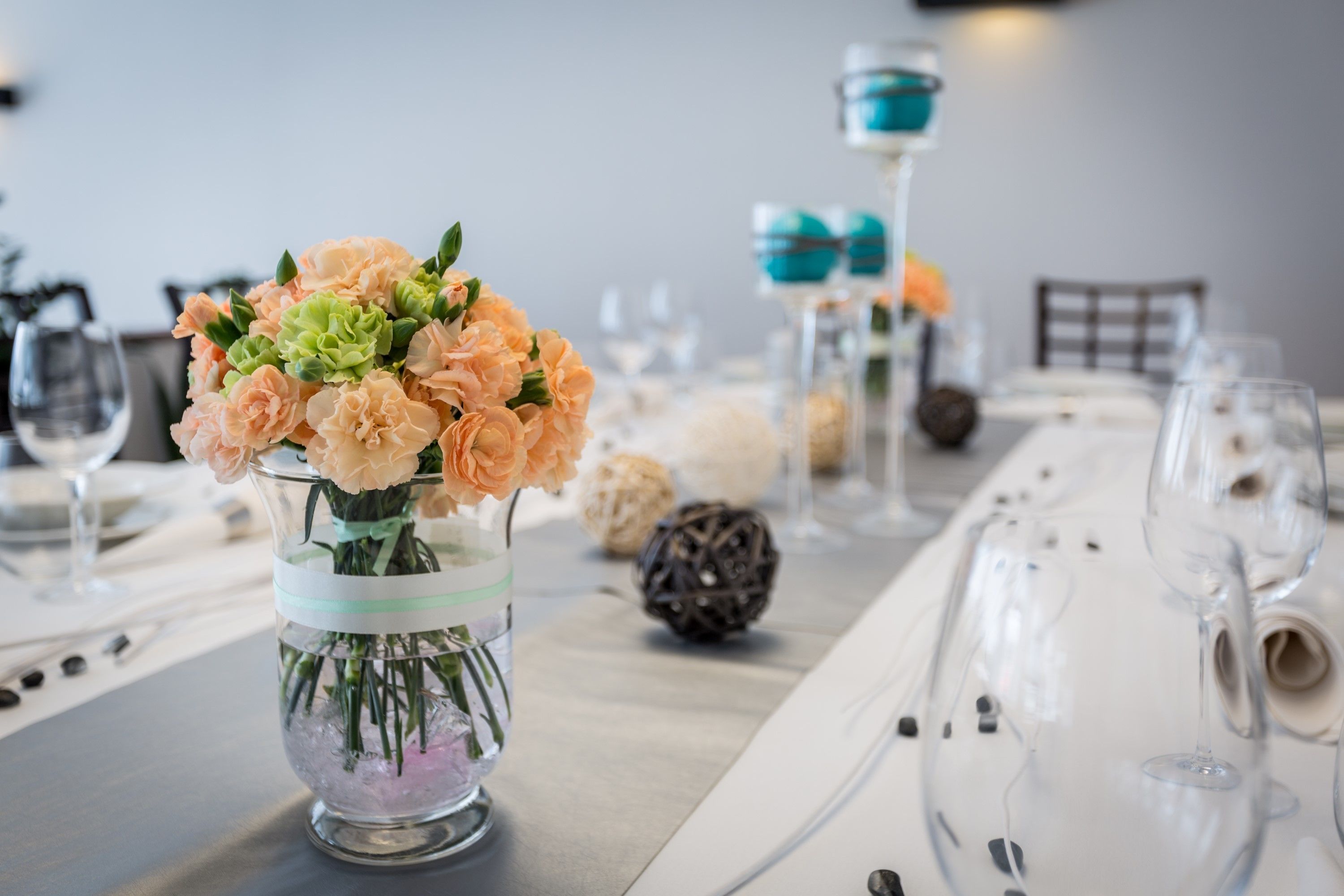 A table set with a clear glass vase containing flowers, a teal-colored candle holder, and a pine cone.
