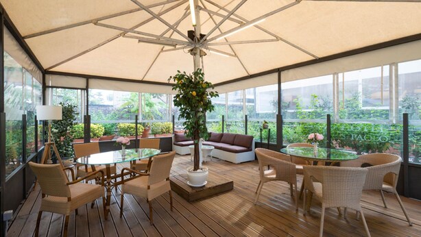 A covered outdoor seating area with a glass table, wicker chairs, and a potted plant. - Hotel San Paolo (Naples)