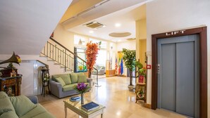 A spacious lobby with a staircase, a green sofa, a glass coffee table, and a lift. - Hotel San Paolo (Naples)