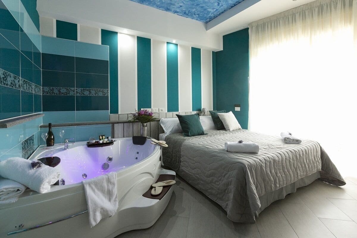 A modern bathroom with a large bathtub, a shower area, and a bed with a grey quilted bedspread.