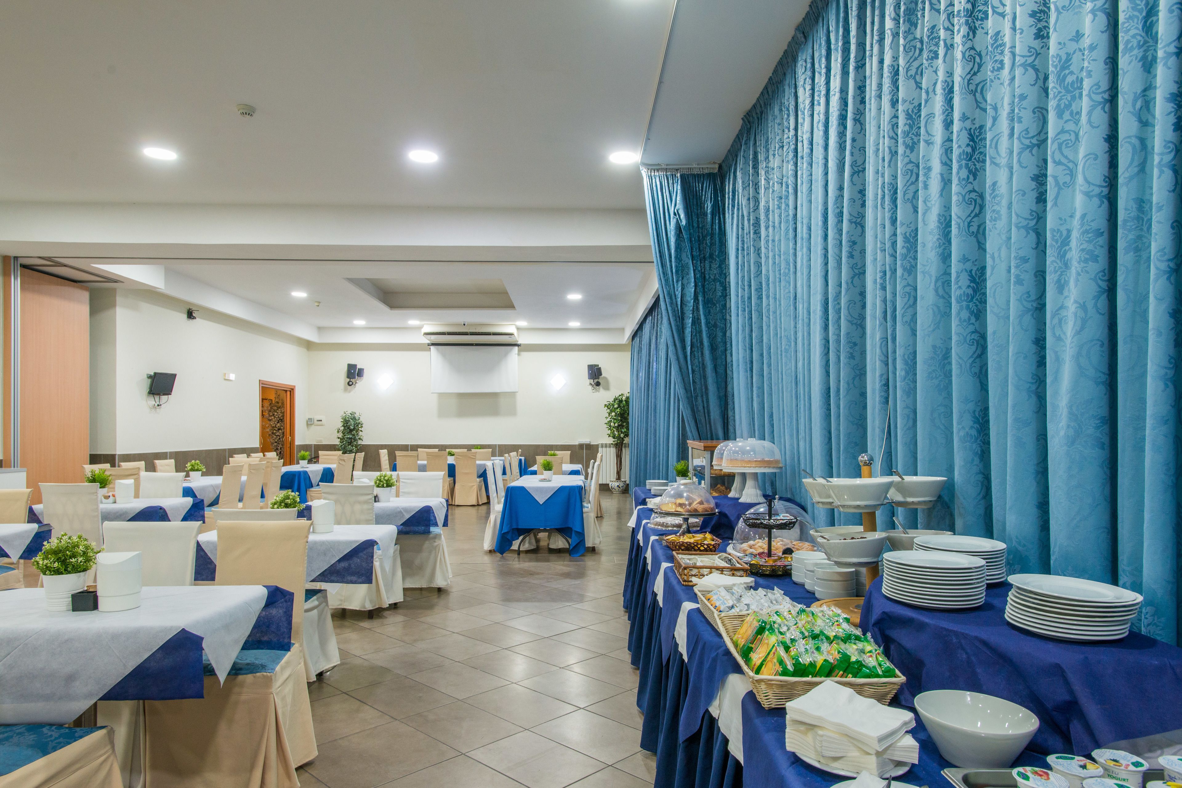 Una sala banchetti con tavoli imbanditi per un buffet, con una varietà di cibi e piatti impilati.
