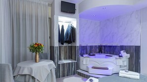 A modern bathroom with a jacuzzi, a vanity with a mirror, and a table with a vase of flowers. - Hotel San Paolo (Naples)