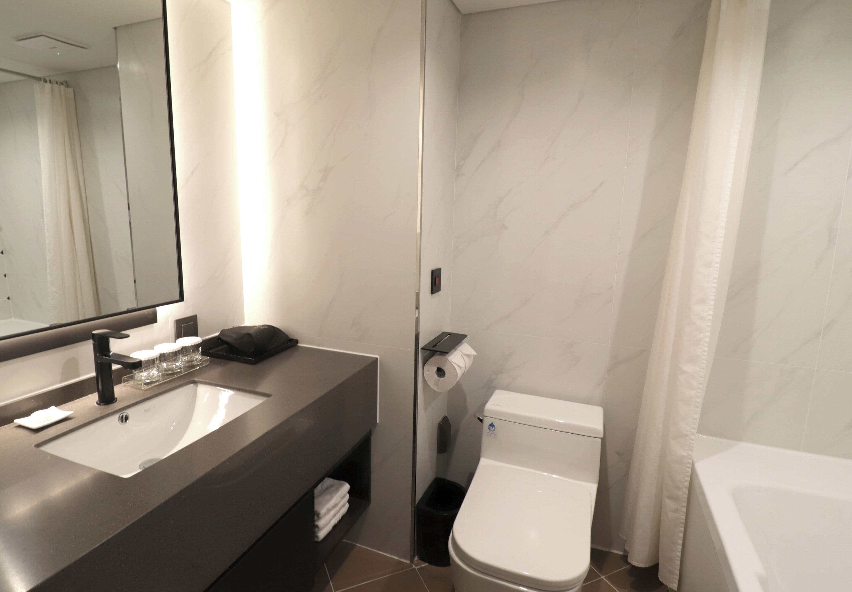 A modern bathroom with a large mirror, a sink, a toilet, and a bathtub.