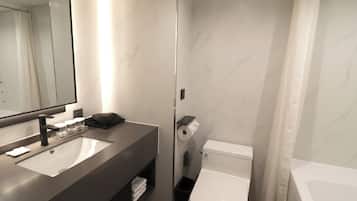 A modern bathroom with a large mirror, a sink, a toilet, and a bathtub.