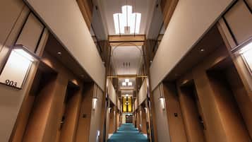A hotel hallway with a blue carpet, wooden doors, and a central light fixture.