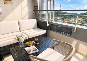 Un balcón con sofá, silla de mimbre, mesa y vistas a un paisaje urbano.