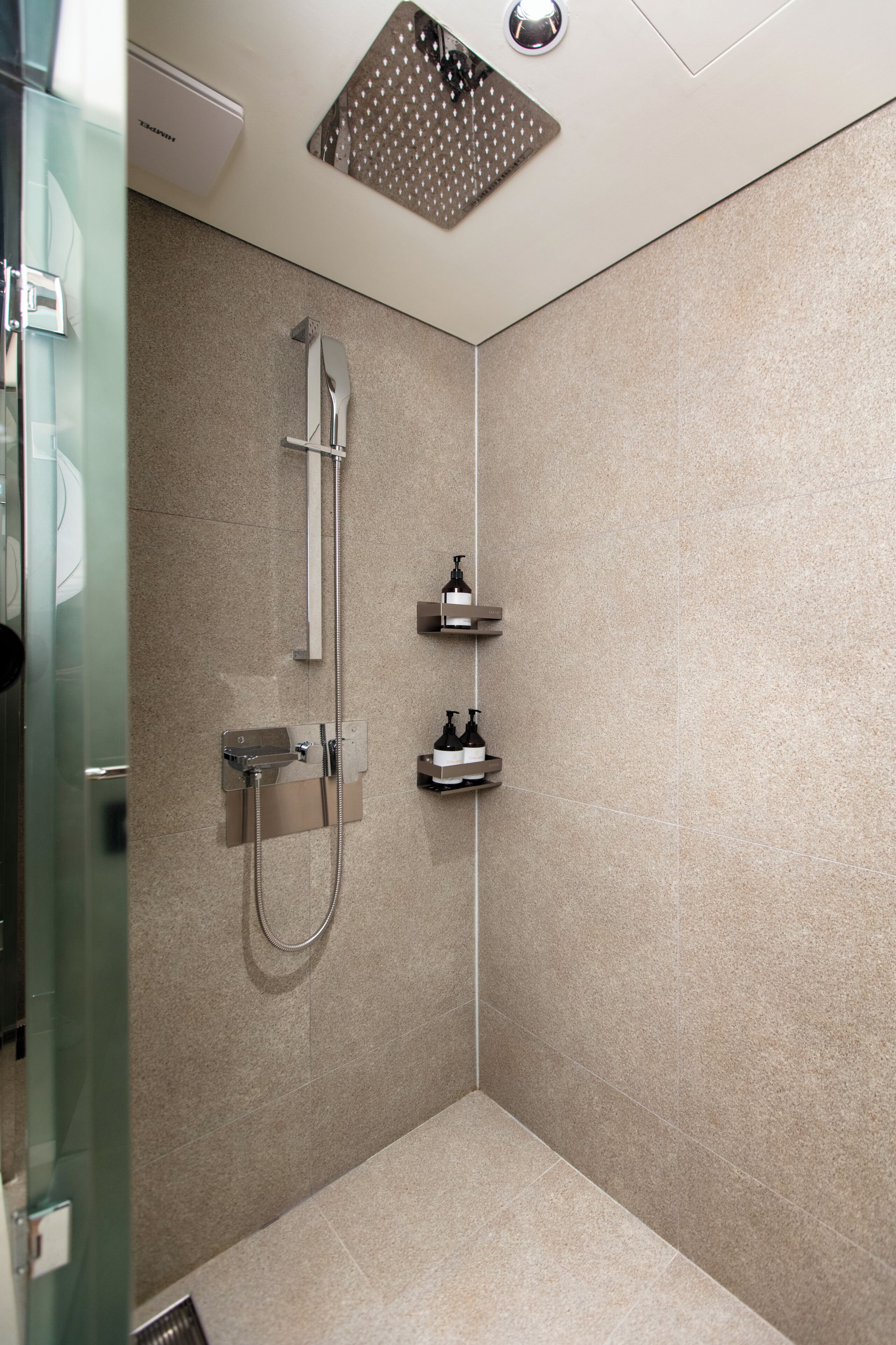 A modern shower with a handheld showerhead, a wall-mounted faucet, and a small shelf with toiletries.