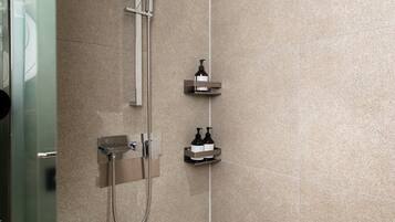 A modern shower with a handheld showerhead, a wall-mounted faucet, and a small shelf with toiletries.