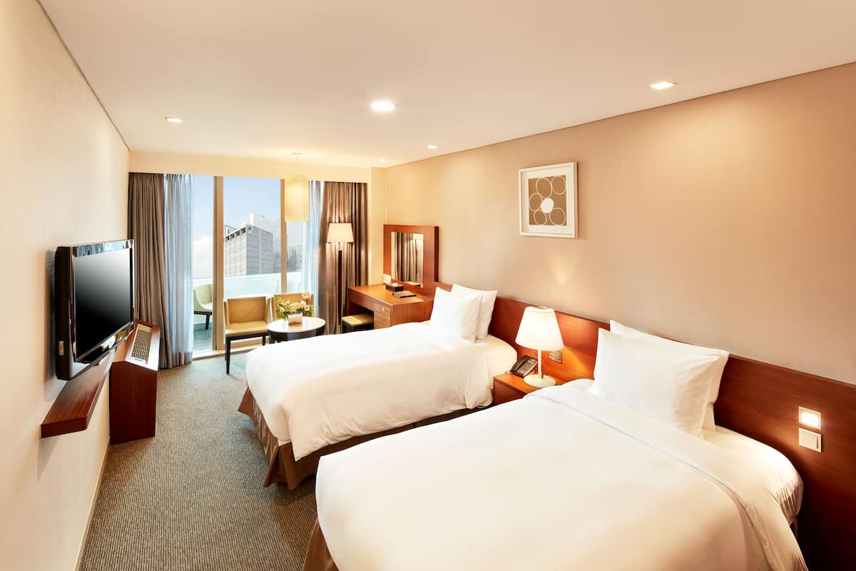A hotel room with two beds, a desk, a TV, and a view of the city.
