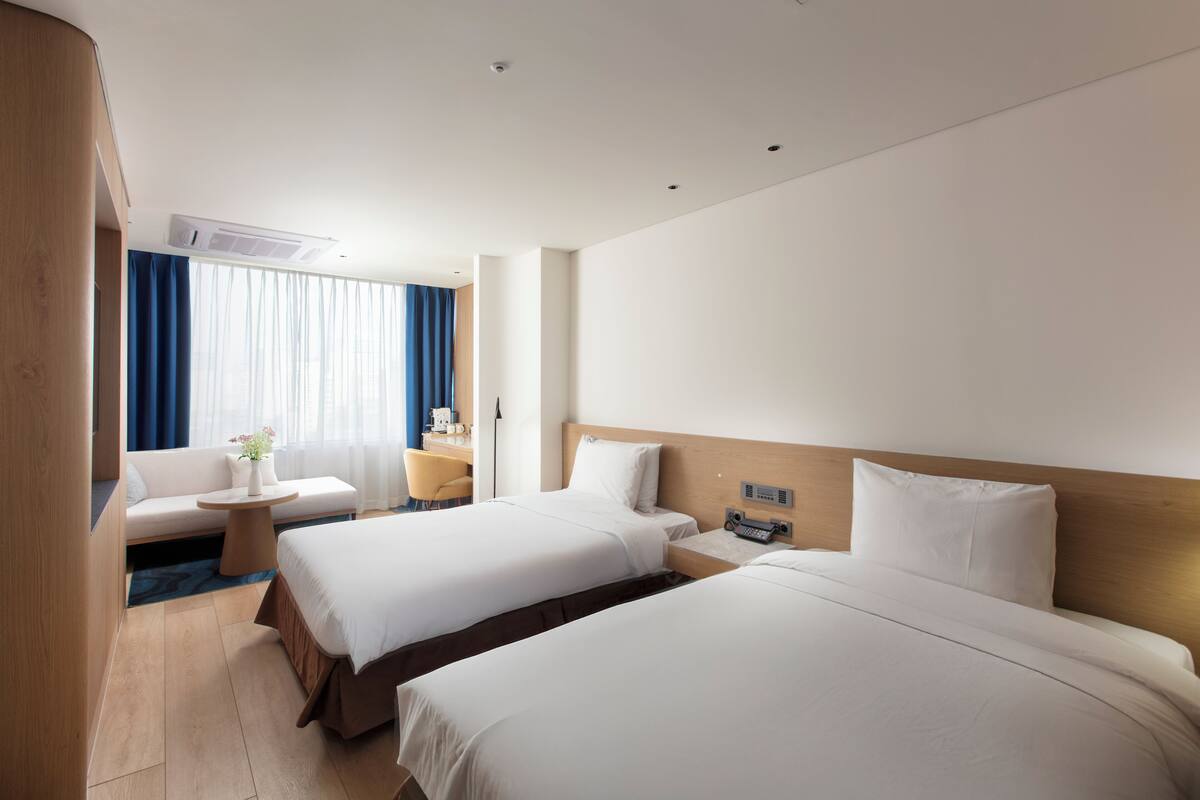 A hotel room with two beds, a sofa, a small table, a desk, and a window with curtains.