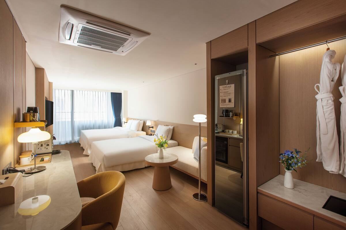 A hotel room with a bed, a desk, a chair, a small table with a vase, and a robe hanging on the wall.